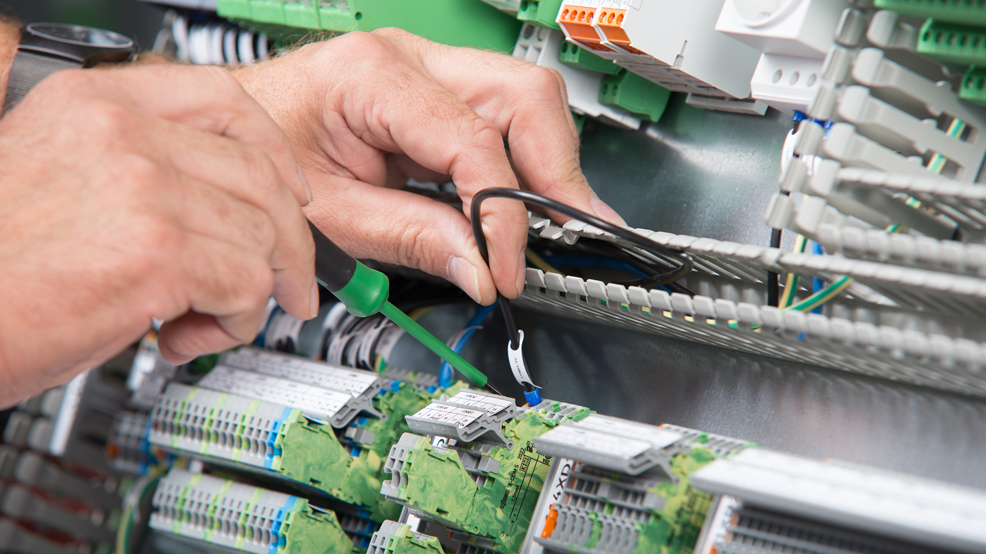 Eine Person mit einem Schraubenzieher verbindet ein schwarzes Kabel mit einer Klemme